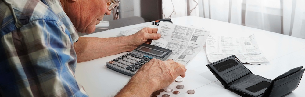 upset senior man sitting at the table and calculating finances. old man checking bills. man counting coins on the table. pension calculation concept