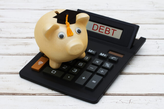 Calculating your student loan debt, A golden piggy bank with a grad hat on a calculator with word Debt over a distressed wood background