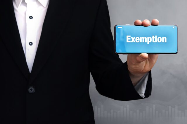 Exemption. Businessman in a suit holds a smartphone at the camera. The term Exemption is on the phone. Concept for business, finance, statistics, analysis, economy
