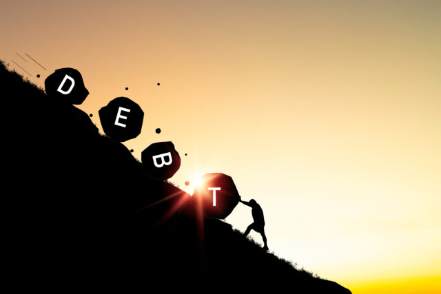 Silhouette of man pushing a debt rock that rolls down a mountain for resist debt and financial freedom concept.
