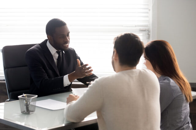 Rear view couple during meeting with African ethnicity family lawyer, spouses and realtor negotiating about rental property, banker worker consulting first real estate purchasing lease mortgage concept
